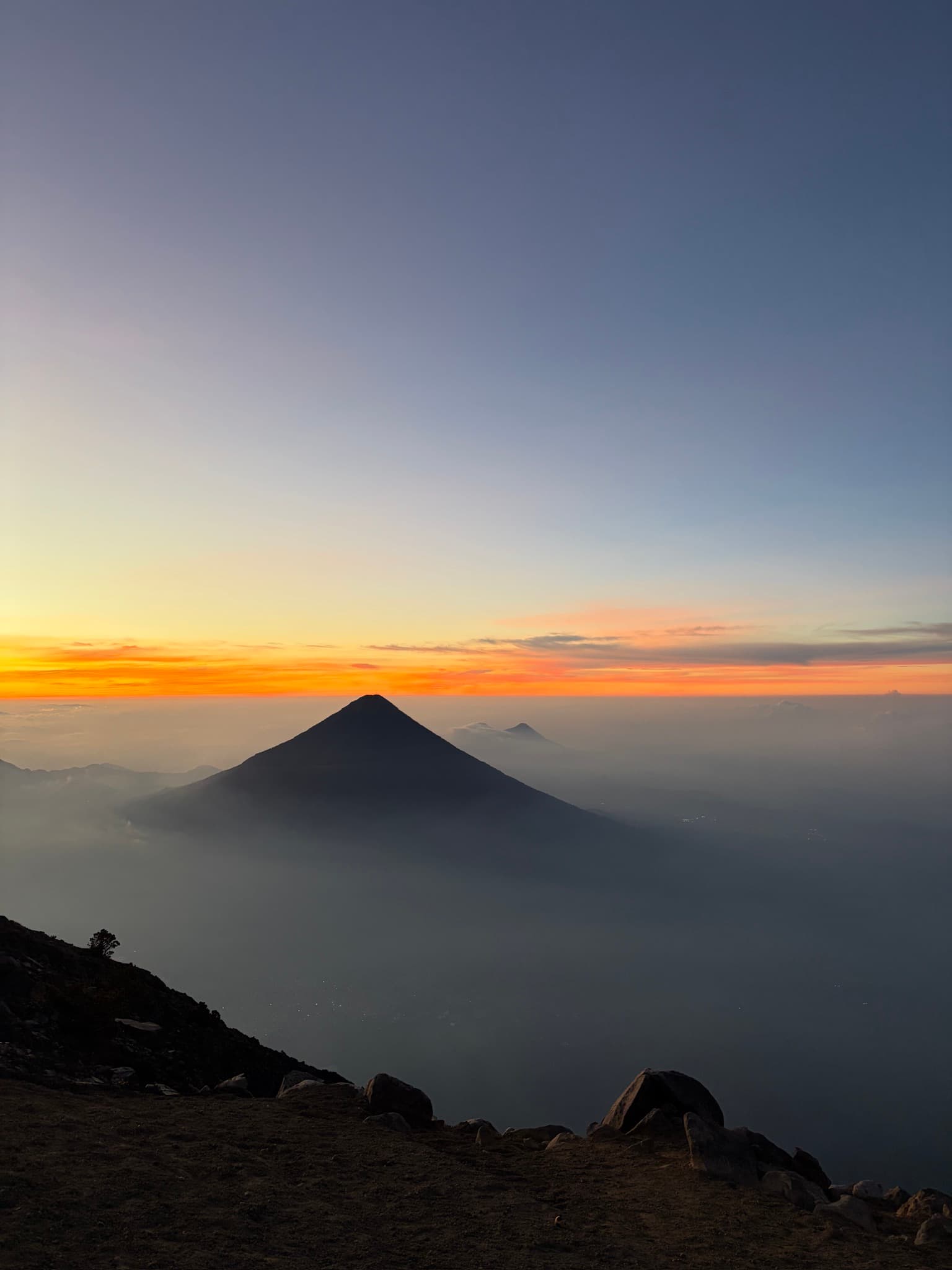 Silhouette of a volcanic peak at sunrise, seen from a ridge above the clouds